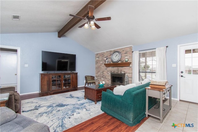 tiled living room featuring vaulted ceiling with beams, visible vents, a ceiling fan, a brick fireplace, and baseboards