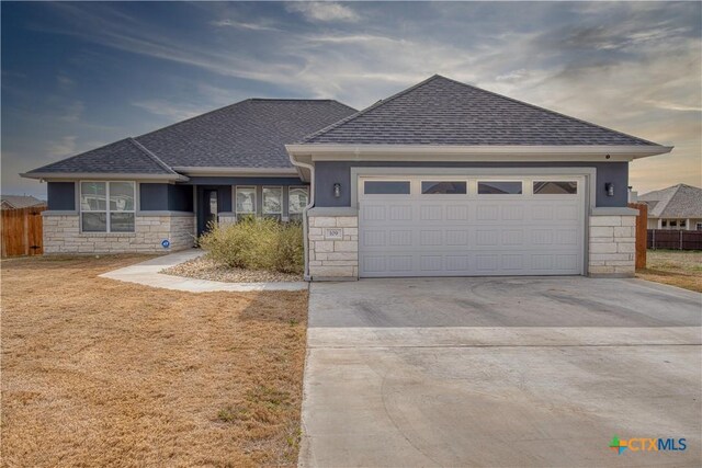 view of front of home featuring a garage, stone siding, driveway, and fence