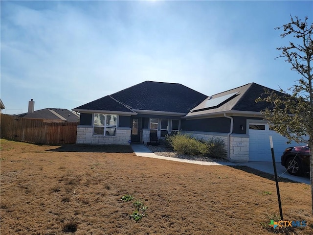 ranch-style home featuring a front yard, fence, an attached garage, stone siding, and roof mounted solar panels