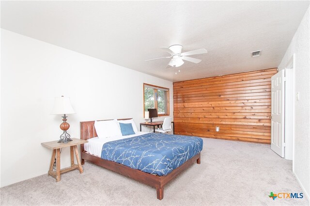 carpeted bedroom featuring wood walls and ceiling fan