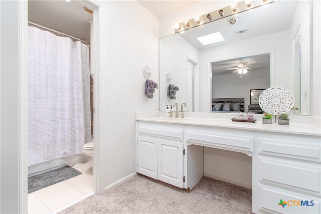 bathroom with ceiling fan, a skylight, vanity, tile patterned floors, and toilet