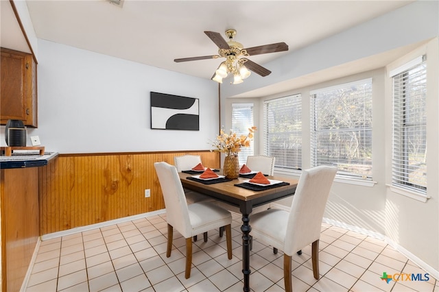 tiled dining space featuring ceiling fan and wood walls