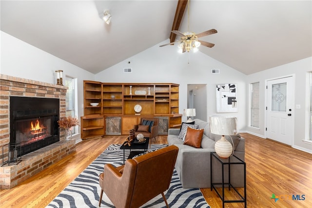 living room with vaulted ceiling with beams, ceiling fan, a fireplace, and light wood-type flooring