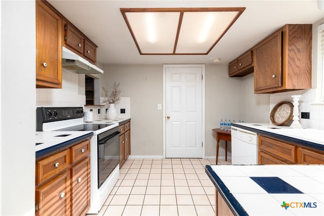 kitchen with tile counters, white appliances, light tile patterned floors, and tasteful backsplash