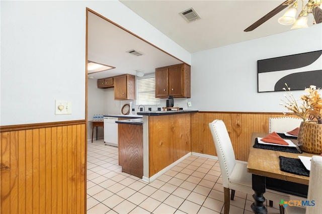 kitchen with kitchen peninsula, ceiling fan, light tile patterned floors, dishwasher, and wood walls