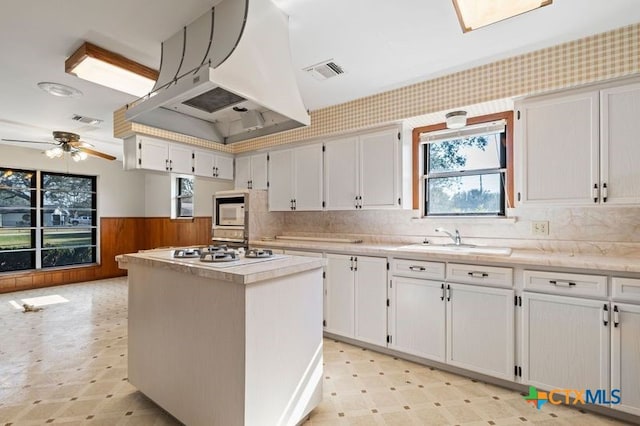 kitchen with stainless steel gas cooktop, sink, island exhaust hood, a kitchen island, and white cabinetry