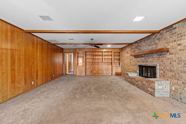 unfurnished living room featuring wood walls, beamed ceiling, carpet, and a brick fireplace