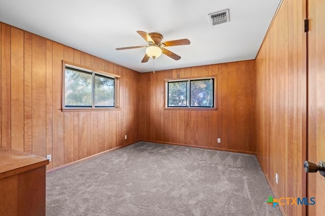 carpeted empty room with wood walls and ceiling fan