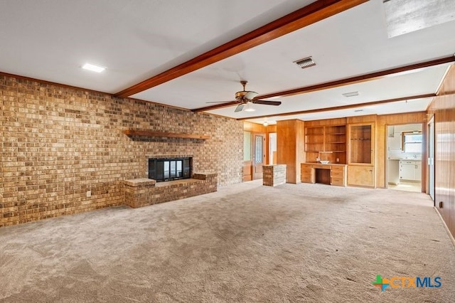 unfurnished living room with a fireplace, beam ceiling, carpet flooring, and brick wall