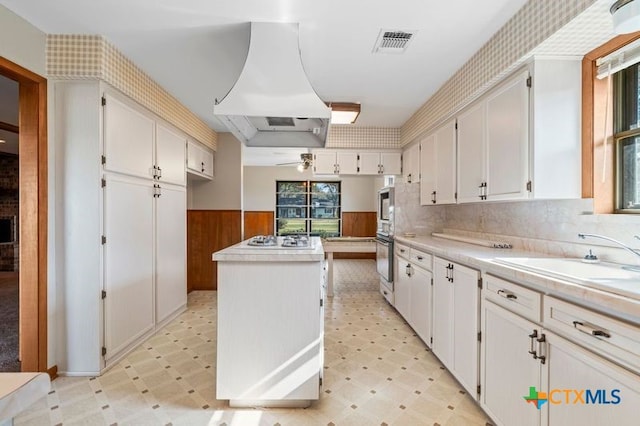 kitchen featuring sink, ventilation hood, white gas cooktop, a kitchen island, and white cabinets