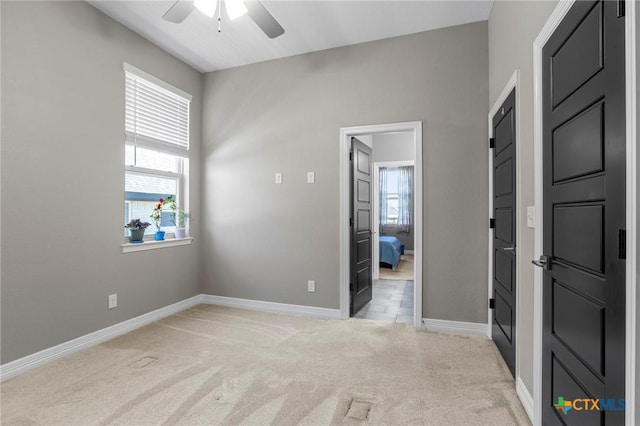 interior space with light colored carpet, a ceiling fan, and baseboards