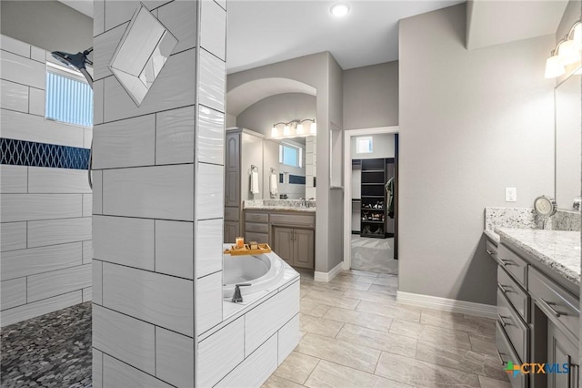 full bathroom featuring a sink, a healthy amount of sunlight, baseboards, two vanities, and a bath
