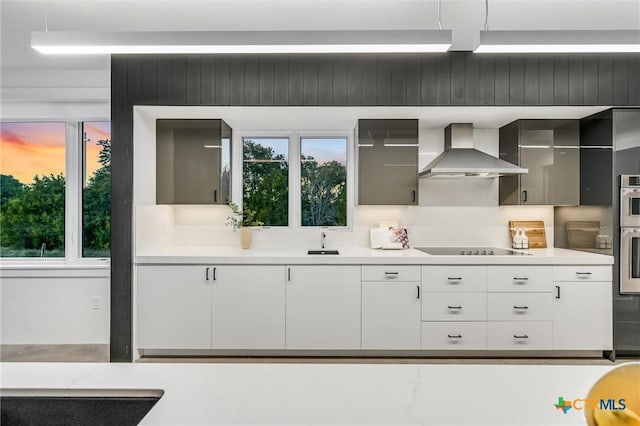 kitchen featuring stainless steel double oven, black electric cooktop, wall chimney exhaust hood, and white cabinets