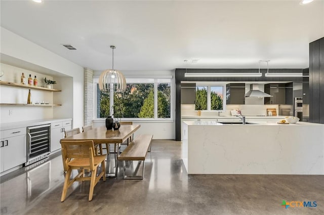 kitchen featuring light stone counters, pendant lighting, wine cooler, wall chimney exhaust hood, and white cabinets