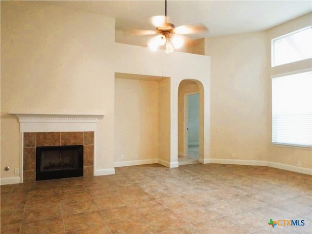 3241 Ranch Park Trl, Round Rock, TX 78681 - unfurnished living room with arched walkways, a ceiling fan, a tiled fireplace, and plenty of natural light