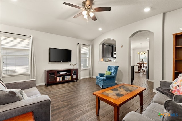 living room with vaulted ceiling, ceiling fan with notable chandelier, a healthy amount of sunlight, and dark hardwood / wood-style floors