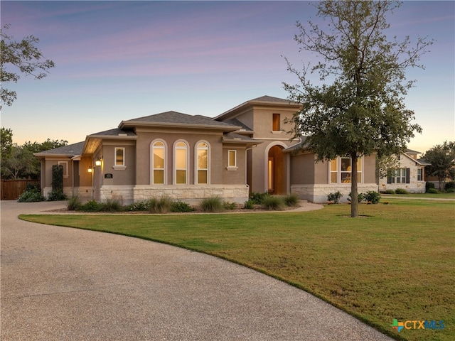 view of front of home with stone siding, a yard, driveway, and stucco siding