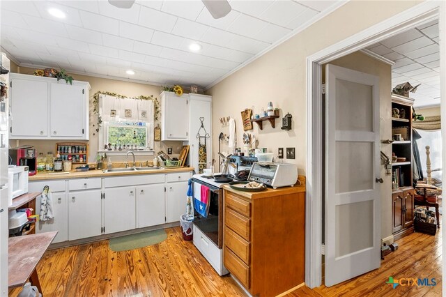 kitchen with light hardwood / wood-style floors, white cabinetry, sink, and crown molding