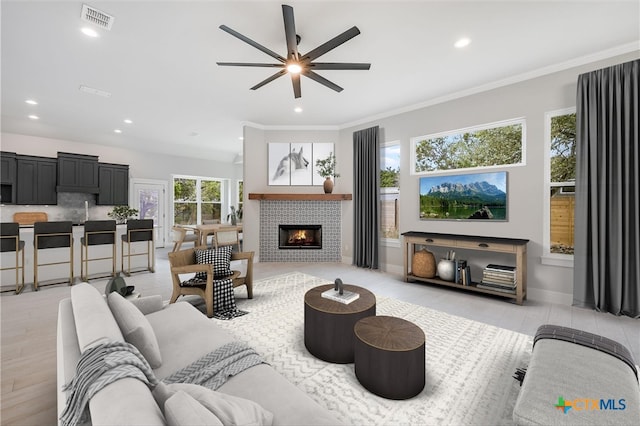 living room with visible vents, a ceiling fan, a tiled fireplace, ornamental molding, and recessed lighting