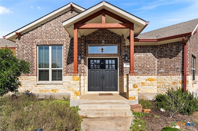 entrance to property featuring stone siding, a shingled roof, and brick siding