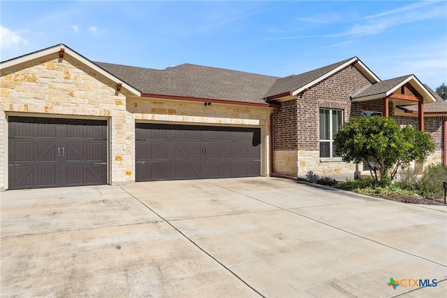 view of front of house with driveway, a garage, stone siding, roof with shingles, and brick siding