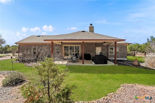 rear view of house with a patio, a chimney, roof with shingles, a yard, and brick siding