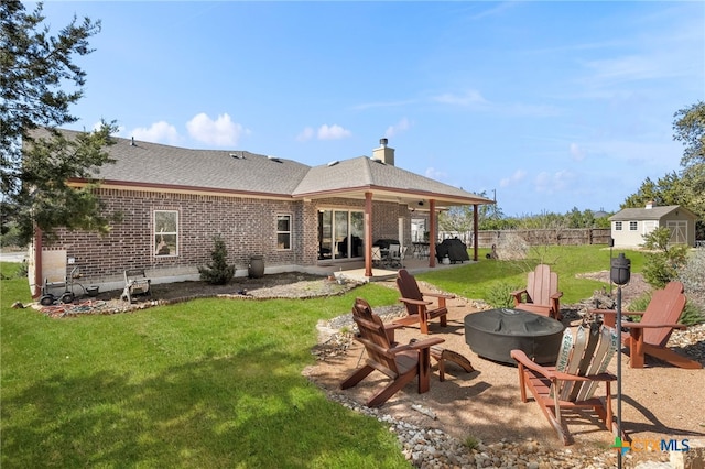 back of house with brick siding, a yard, a patio, an outdoor fire pit, and fence