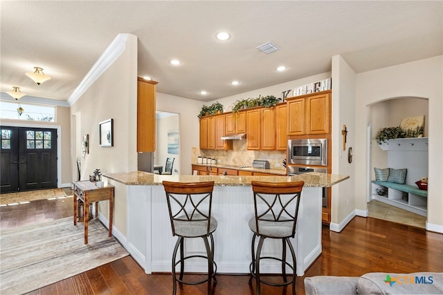 kitchen with tasteful backsplash, dark wood-style floors, a breakfast bar area, a peninsula, and stainless steel appliances