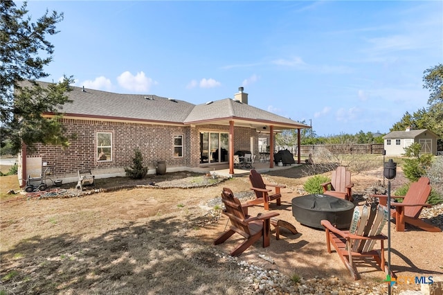 rear view of property with brick siding, a patio, a fire pit, and fence