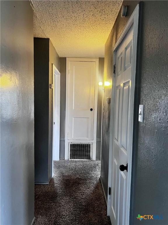 corridor with a textured ceiling and dark colored carpet