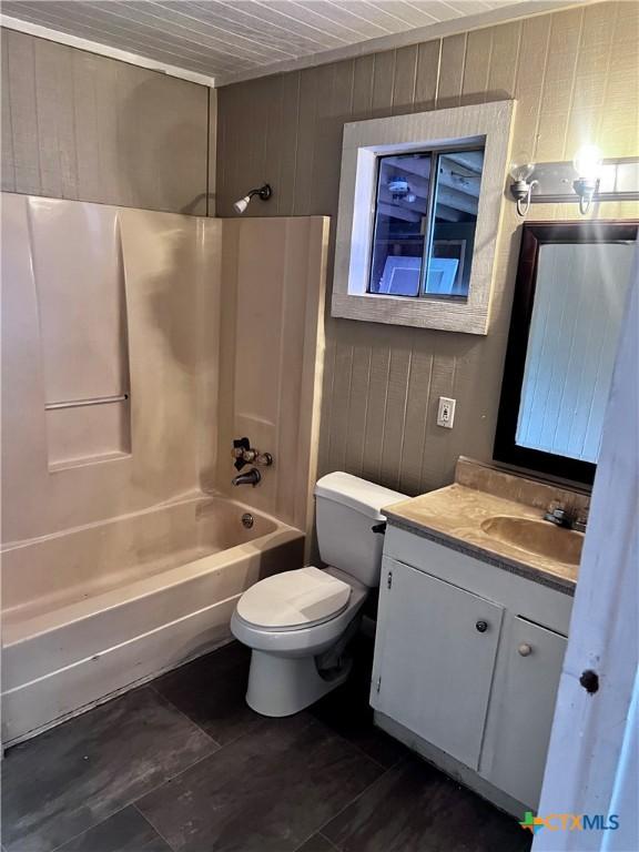 full bathroom with toilet, shower / bath combination, wooden walls, and vanity