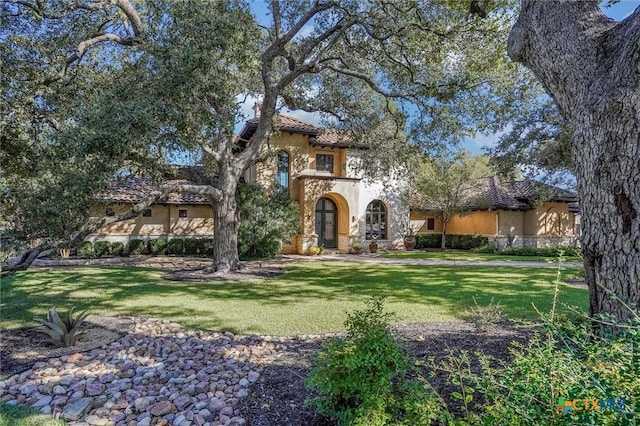 mediterranean / spanish house featuring stone siding, a front yard, a tile roof, and stucco siding