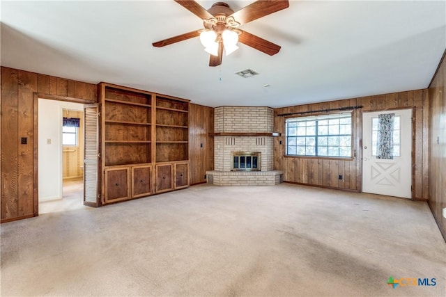 unfurnished living room featuring carpet floors, wood walls, plenty of natural light, and a brick fireplace