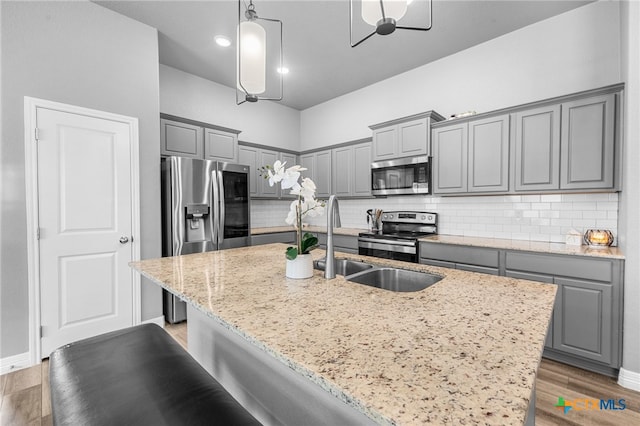 kitchen featuring stainless steel appliances, a kitchen island with sink, wood-type flooring, and pendant lighting