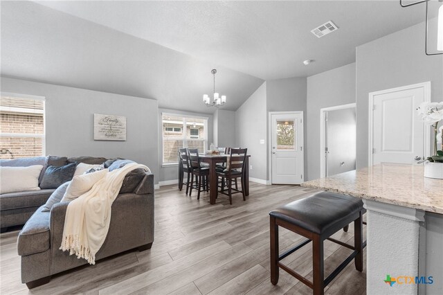 living room with light hardwood / wood-style floors, plenty of natural light, vaulted ceiling, and a notable chandelier