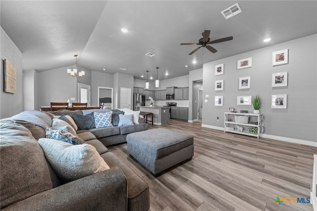 living room featuring lofted ceiling, hardwood / wood-style flooring, and ceiling fan with notable chandelier