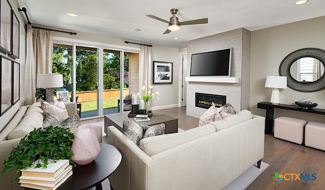 living room featuring dark wood-type flooring, ceiling fan, and a tile fireplace