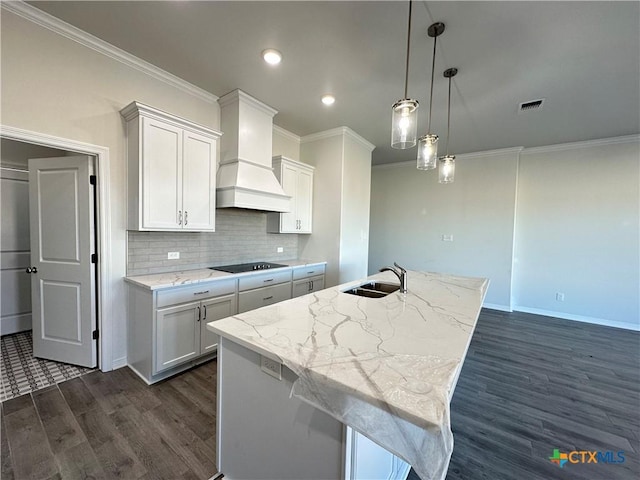 kitchen with custom exhaust hood, sink, hanging light fixtures, a kitchen island with sink, and white cabinets