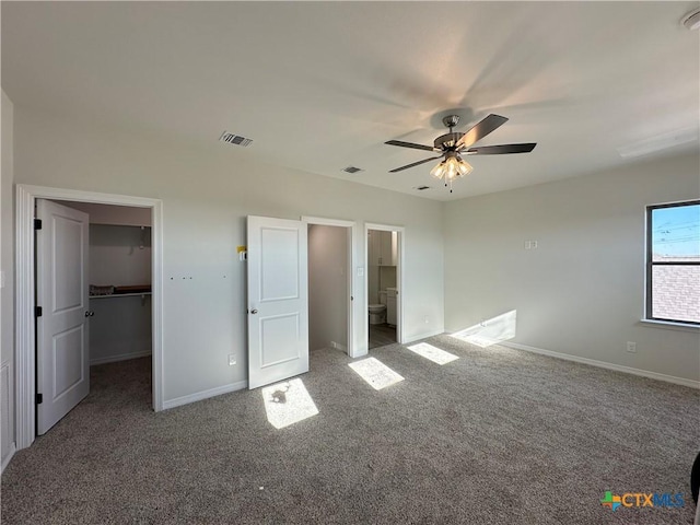 unfurnished bedroom with a spacious closet, a closet, ceiling fan, dark carpet, and ensuite bathroom