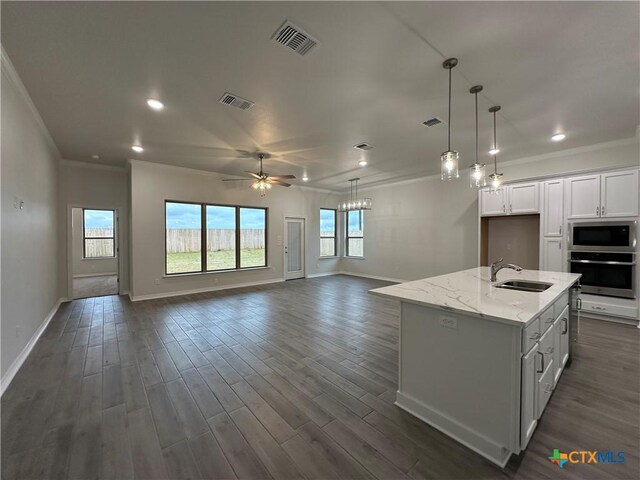 kitchen featuring white cabinets, decorative light fixtures, oven, a center island with sink, and custom range hood