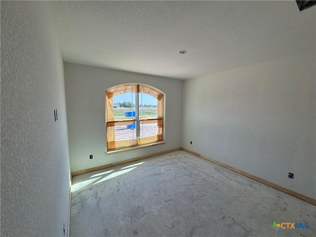 spare room featuring a textured ceiling, a textured wall, baseboards, and unfinished concrete floors