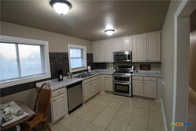 kitchen with light tile patterned floors, stainless steel appliances, white cabinetry, and sink