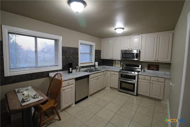 kitchen with sink, a textured ceiling, light tile patterned flooring, white cabinetry, and stainless steel appliances