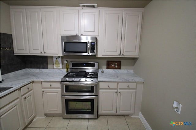 kitchen with light tile patterned floors, white cabinetry, light stone counters, and appliances with stainless steel finishes