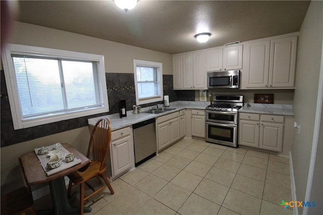 kitchen with white cabinets, appliances with stainless steel finishes, light tile patterned floors, and sink