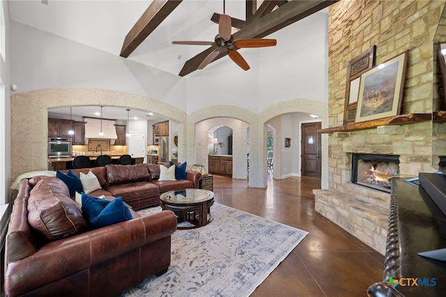 1448 Decanter Dr, New Braunfels, TX 78132 - living room featuring arched walkways, high vaulted ceiling, a ceiling fan, a fireplace, and beam ceiling