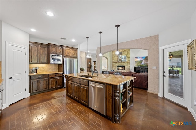 1448 Decanter Dr, New Braunfels, TX 78132 - kitchen with appliances with stainless steel finishes, dark brown cabinetry, an island with sink, a stone fireplace, and backsplash
