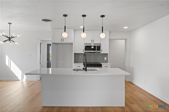 kitchen featuring a kitchen island with sink, light hardwood / wood-style floors, white cabinetry, and tasteful backsplash