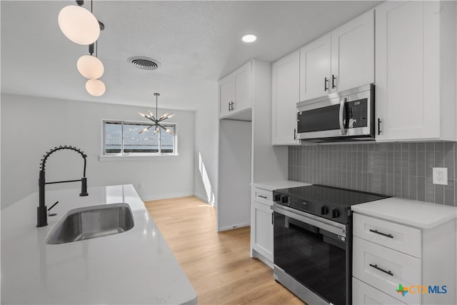 kitchen with appliances with stainless steel finishes, hanging light fixtures, decorative backsplash, sink, and white cabinets