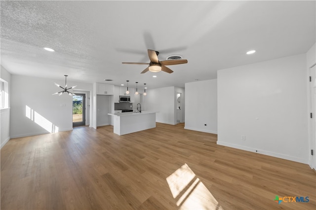 unfurnished living room with a textured ceiling, ceiling fan with notable chandelier, light hardwood / wood-style floors, and sink